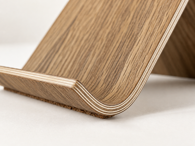 Close-up of the Ray phone stand with visible layered plywood edges and a natural wood grain finish on a light neutral background.
